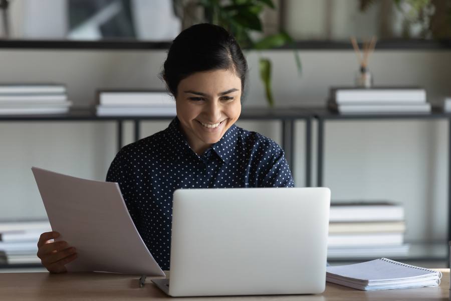 Woman holding paper and smiling at laptop